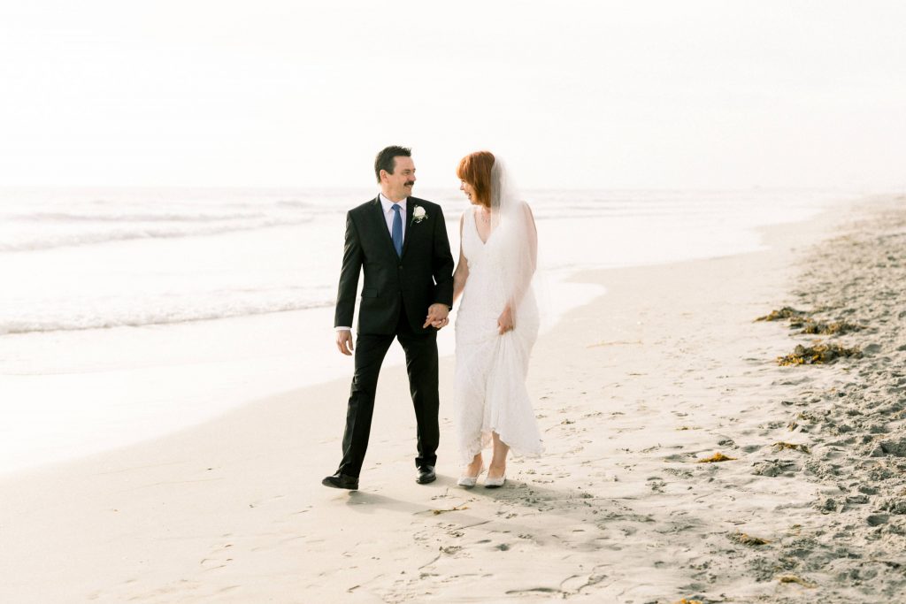 bride and groom walking together holding hands on the beach laughing Magee park wedding in Carlsbad California Cynthia and James wedding engagement photography Carrie McGuire photographer 