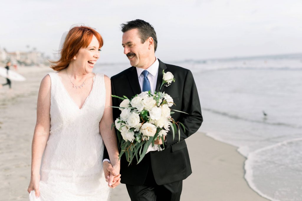 happy newlyweds walking and laughing on the beach Magee park wedding in Carlsbad California Cynthia and James wedding engagement photography Carrie McGuire photographer 