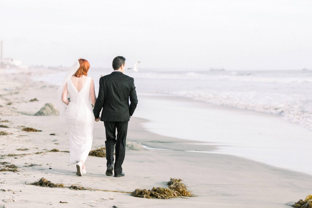 newlywed couple walking away on the beach looking at the ocean Magee park wedding in Carlsbad California Cynthia and James wedding engagement photography Carrie McGuire photographer 